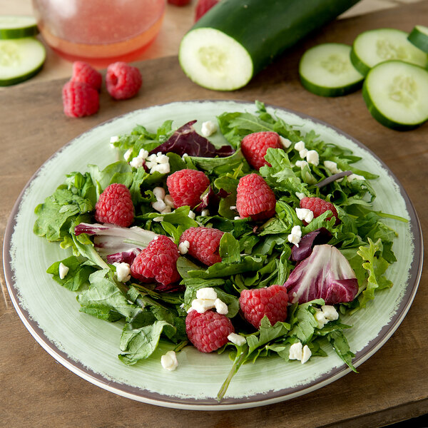 A Carlisle jade melamine salad plate with a salad of raspberries and cucumbers.