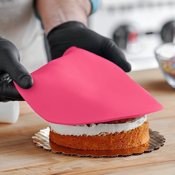 A person wearing black gloves and using a pink cloth to smooth Satin Ice pink fondant on a cake.
