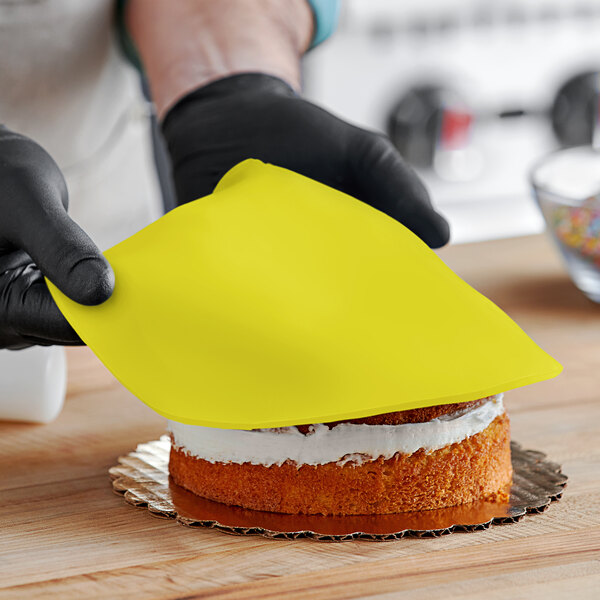 A person wearing black gloves and using a yellow cloth to smooth Satin Ice yellow rolled fondant over a cake.