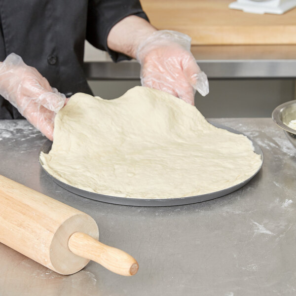 A person in gloves using a rolling pin to flatten dough on an American Metalcraft Super Perforated Pizza Pan.