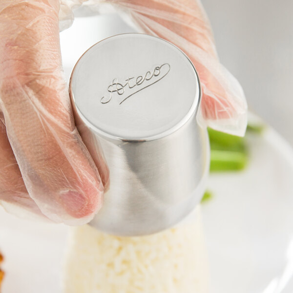 A person using a silver Ateco stainless steel food mold to make a cake.