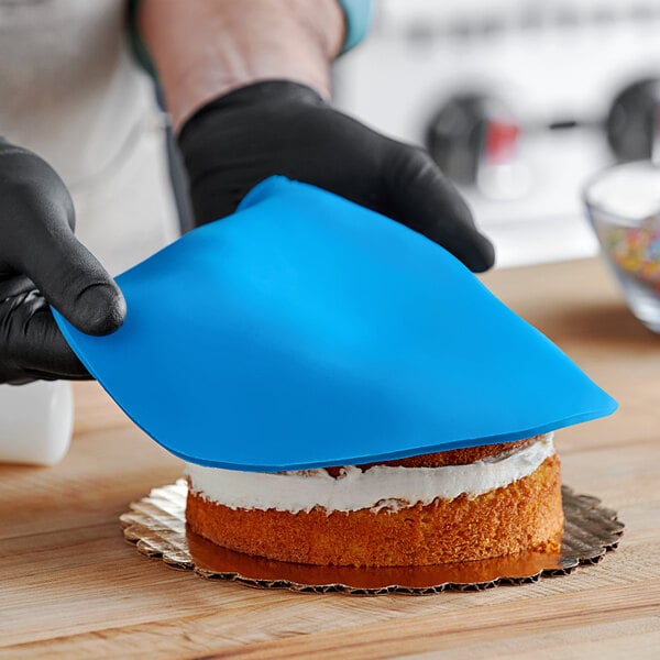 A person wearing black gloves and holding blue Satin Ice fondant over a cake.
