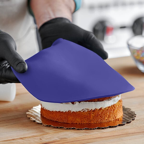 A person wearing black gloves and holding a blue cloth over a Satin Ice Purple Vanilla Rolled Fondant cake