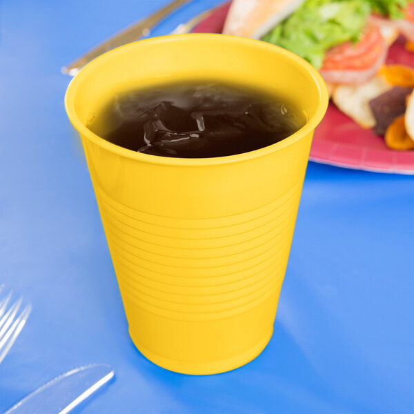 A School Bus Yellow plastic cup filled with liquid on a table next to a plate of food.