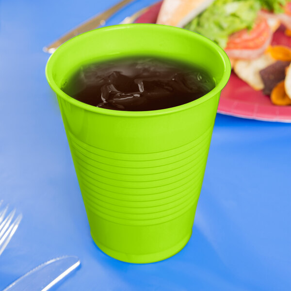 A close up of a green Creative Converting plastic cup with liquid in it.