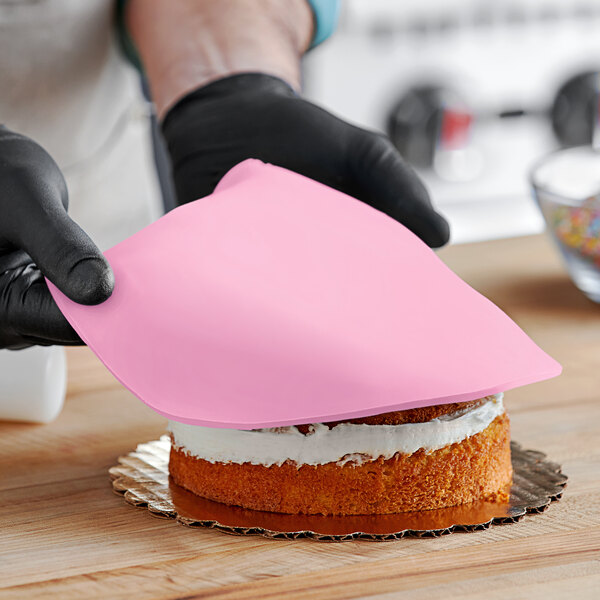 A person wearing black gloves and using a pink satin cloth to cover a cake with Satin Ice Baby Pink Rolled Fondant.