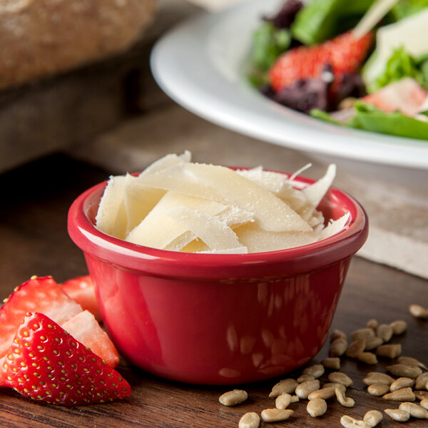 A white table with a bowl of cheese and strawberries in a Carlisle red melamine ramekin.