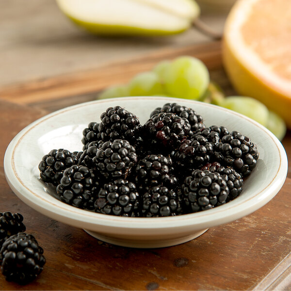A Carlisle Grove melamine fruit bowl filled with blackberries on a table.