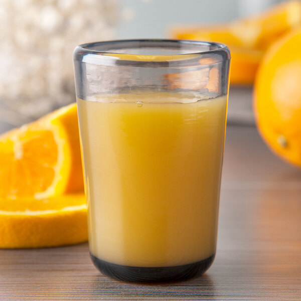 A Carlisle Mingle Tritan plastic juice glass filled with orange juice on a table with oranges.