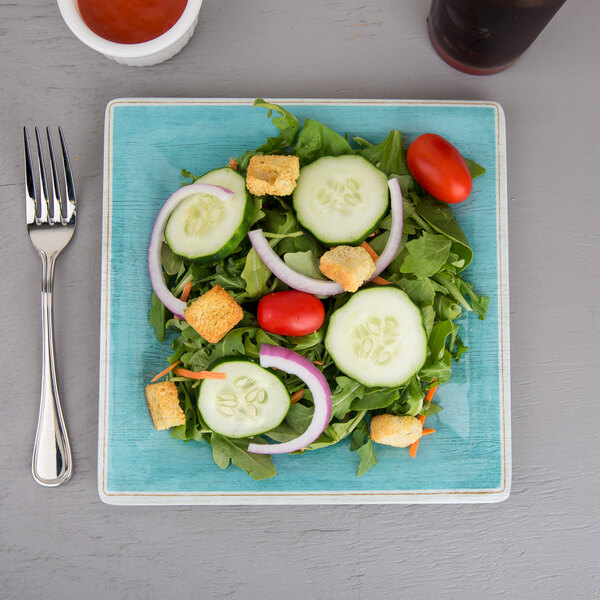 A Carlisle Grove aqua melamine salad plate with a salad, a cracker, and a glass of soda on a table.