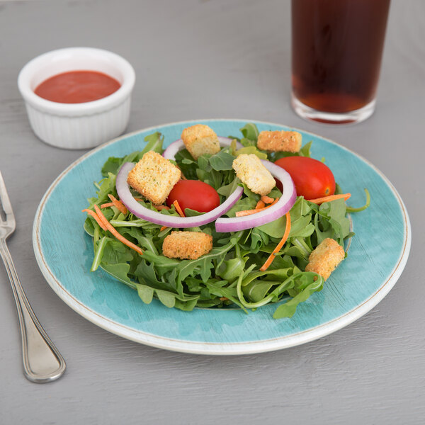A Carlisle Aqua melamine salad plate with a salad next to a glass of soda.