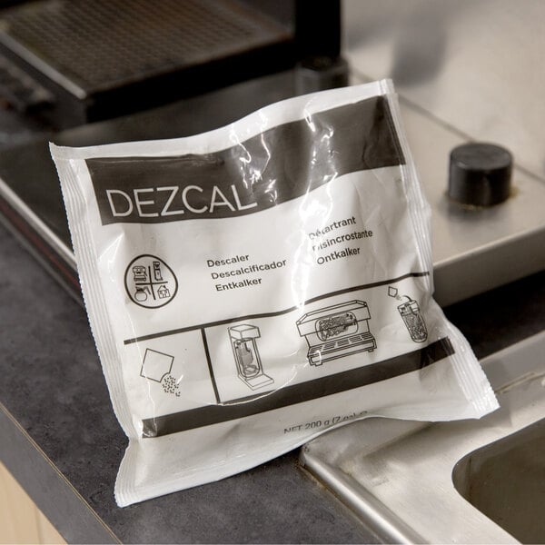 A white bag of Urnex Dezcal coffee equipment scale removing powder on a counter next to a sink.