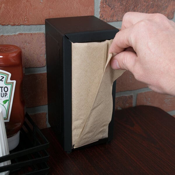A hand putting a Choice Kraft Natural Tall-Fold dispenser napkin in a black dispenser box.