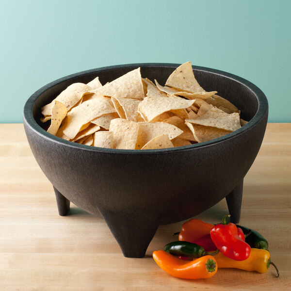 A charcoal polypropylene molcajete filled with tortilla chips and peppers on a table.