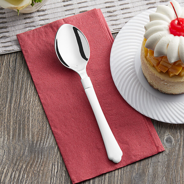 A Visions white plastic spoon on a plate with cake on a napkin.