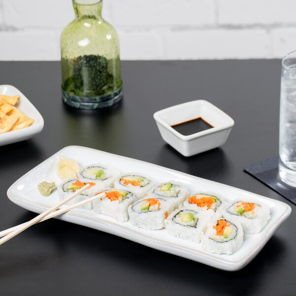 A rectangular white china tray with sushi and chopsticks on it.