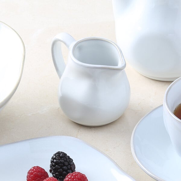 A white pitcher on a marble surface with a Tuxton Artisan Agave creamer filled with berries.