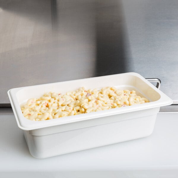 A white Cambro food pan containing macaroni and cheese on a school kitchen counter.