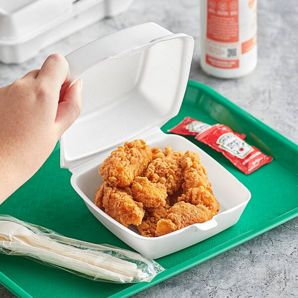 A hand holding a white Dart foam container of chicken.