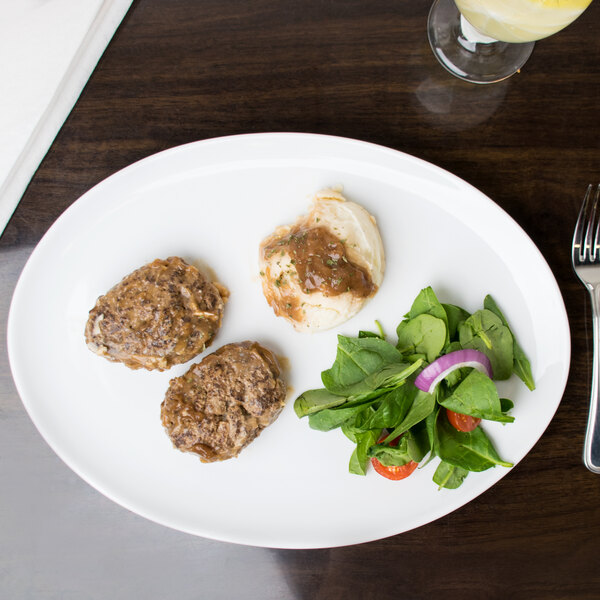 An Arcoroc white porcelain oval platter with three meat patties and a salad on a table.