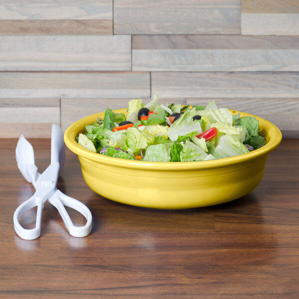 A Fiesta Sunflower china bowl filled with salad on a table next to a pair of scissors.