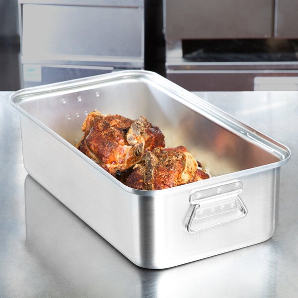 A Vollrath Wear-Ever aluminum roasting pan with meat inside on a counter.