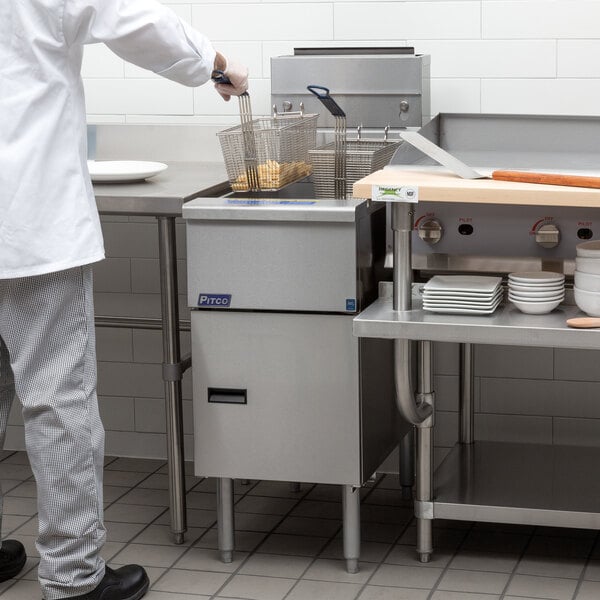 A chef in a white uniform using a Pitco Solstice natural gas floor fryer.