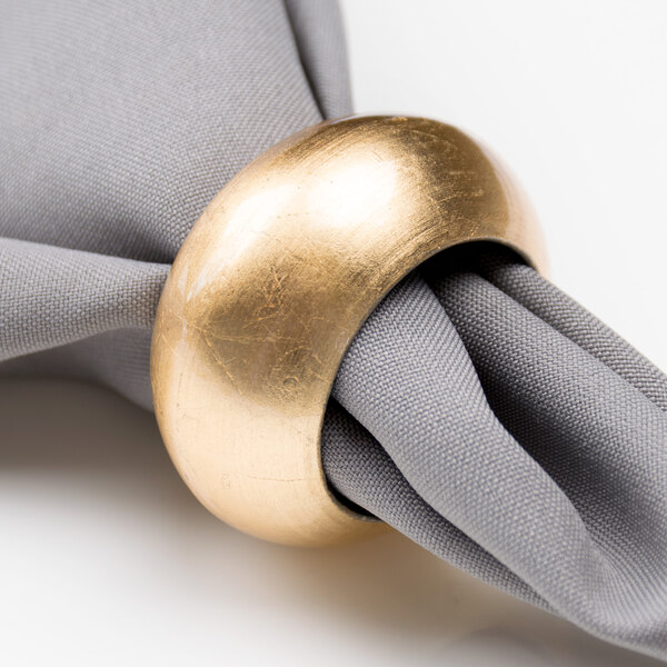 An American Atelier gold acrylic napkin ring on a gray napkin.