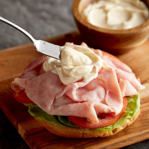 A sandwich with ham and cheese and AAK Select Recipe mayonnaise on a cutting board.