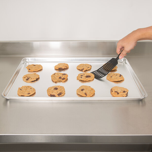 A hand using a spatula to make cookies on a Vollrath bun / sheet pan.