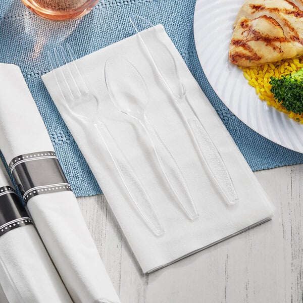 A white napkin and clear plastic fork, knife, and spoon on a plate.