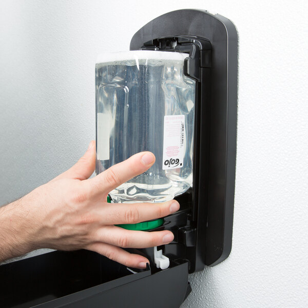 A person's hand using GOJO Clear & Mild foaming hand soap from a wall mounted dispenser.
