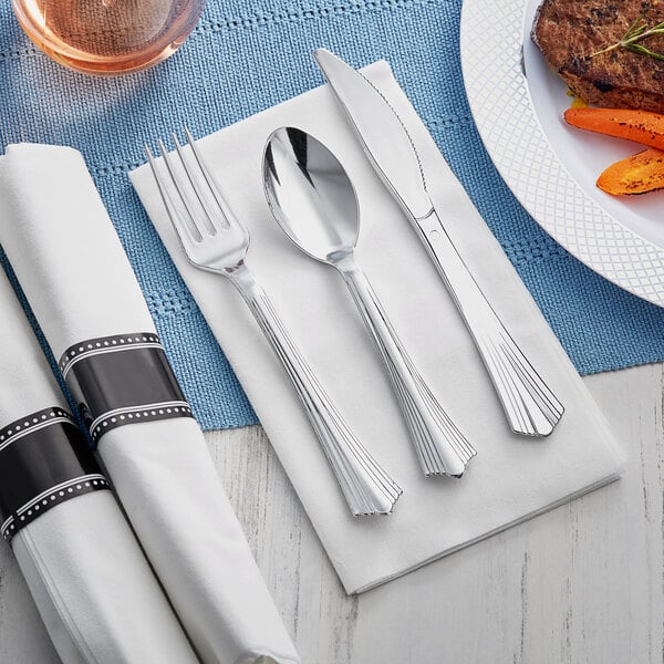 A Visions pre-rolled napkin with silver heavy weight plastic cutlery on a white napkin next to a plate of carrots.