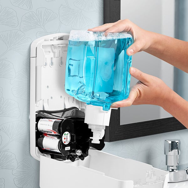 A person washing their hands with GOJO foaming hand soap in a clear dispenser with blue liquid.