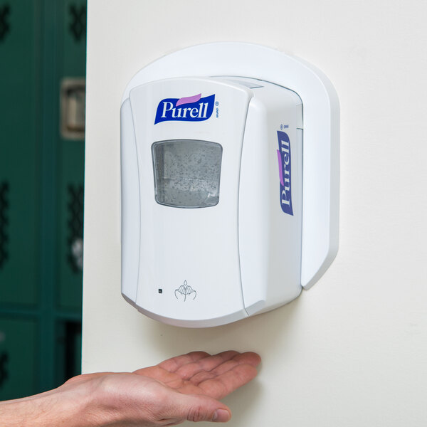 A hand using a Purell LTX hand sanitizer dispenser.