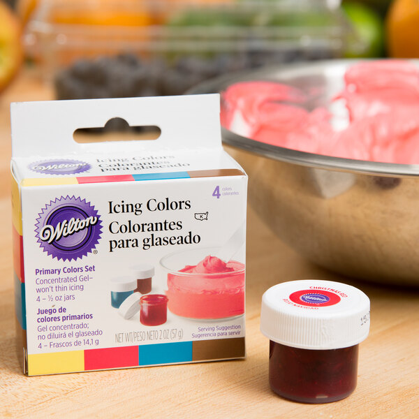 A container of Wilton Primary Gel Food Coloring next to a bowl of pink frosting.