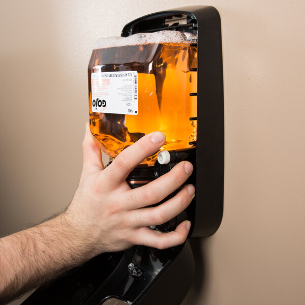 A hand holding a GOJO TFX dispenser with amber liquid in it.