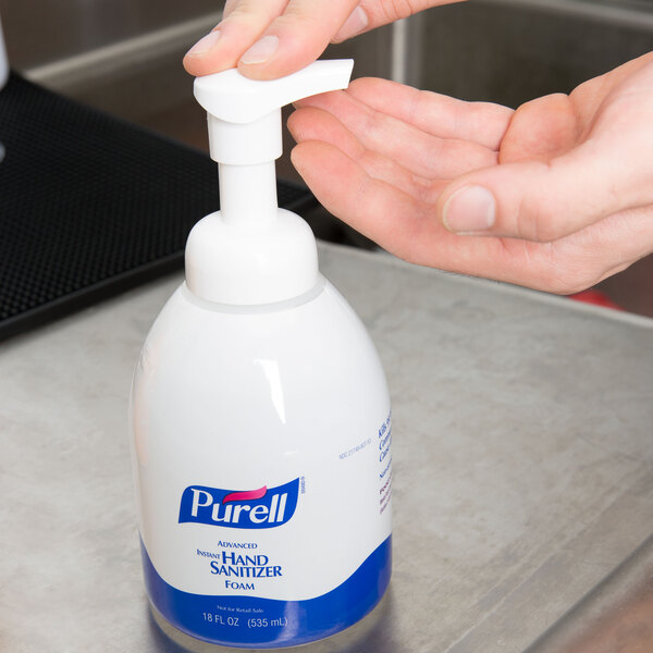 A hand using a Purell hand sanitizer pump.