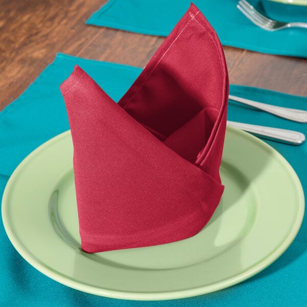 A folded hot pink Intedge cloth napkin on a plate with a fork and knife.