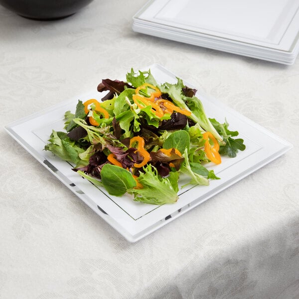 A Fineline white plastic square plate with salad on it on a table.