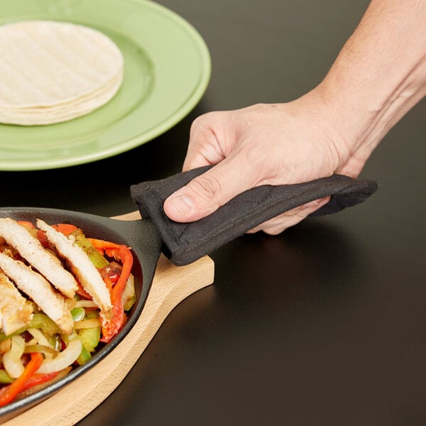 A hand holding a Choice black cotton handle cover over a pan of food.