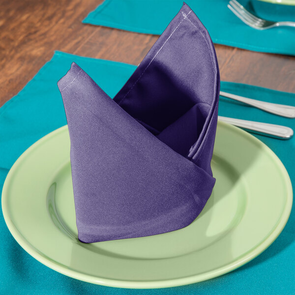 A folded purple Intedge cloth napkin on a plate with silverware.