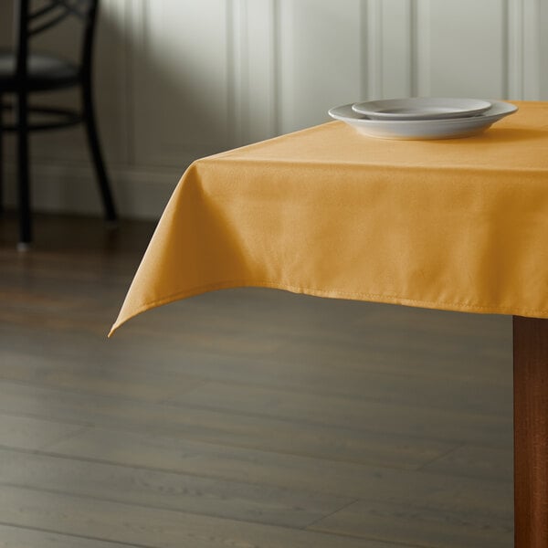 A square gold polyester table cover on a table with plates on it.