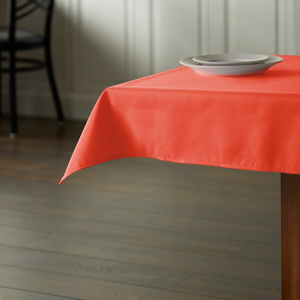 An orange Intedge cloth table cover on a square table with a plate on it.