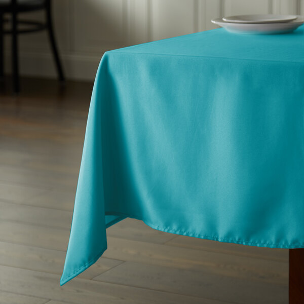 A square teal tablecloth on a table in a restaurant.