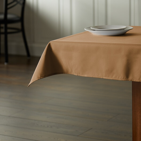 A table with a beige Intedge square tablecloth and plates on it.