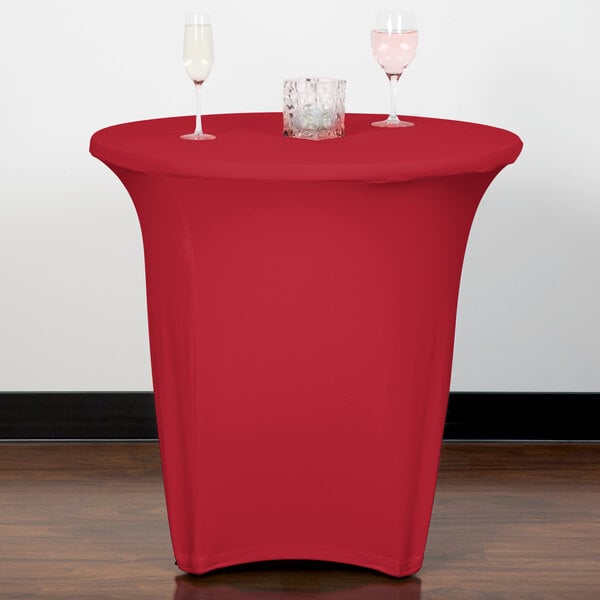A table with a Snap Drape crimson spandex table cover and two wine glasses on it.