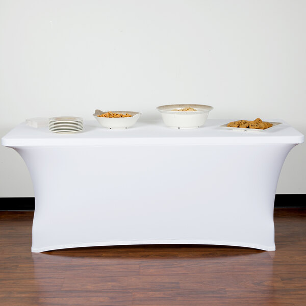 A wood table with white Snap Drape spandex table cover with plates and bowls of food.