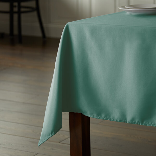 A table with a seafoam green square tablecloth on it.