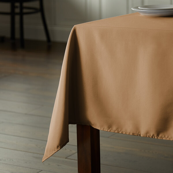 A table with a rectangular beige Intedge cloth table cover on it.